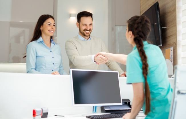 Dental office receptionist shaking hands with a patient at front desk