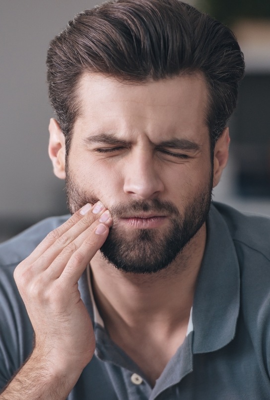 Wincing man holding his cheek in pain needing emergency dentist in Federal Way