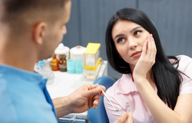 Woman holding her cheek in pain while talking to her emergency dentist