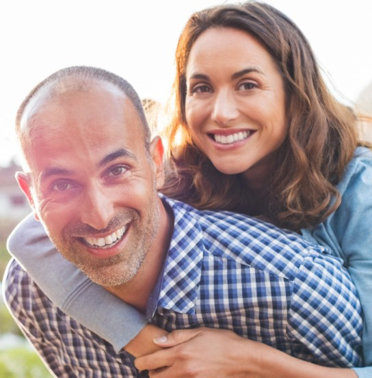 Smiling woman hugging man from behind outdoors