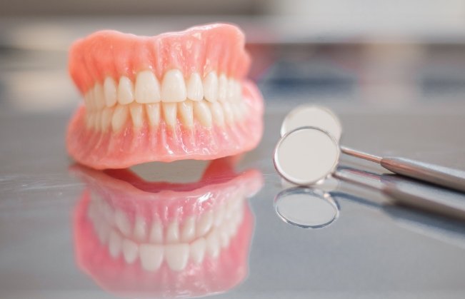 Set of full dentures on tray next to dental mirrors