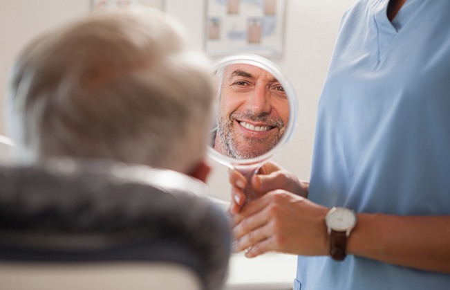 A dentist showing their patient their smile with a hand mirror