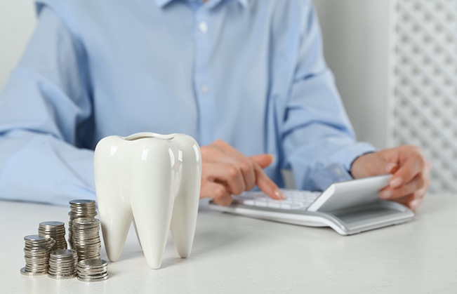 A patient using a calculator next to a model tooth and stacks of coins