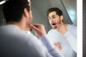 Man examining a bump on his gums in the mirror